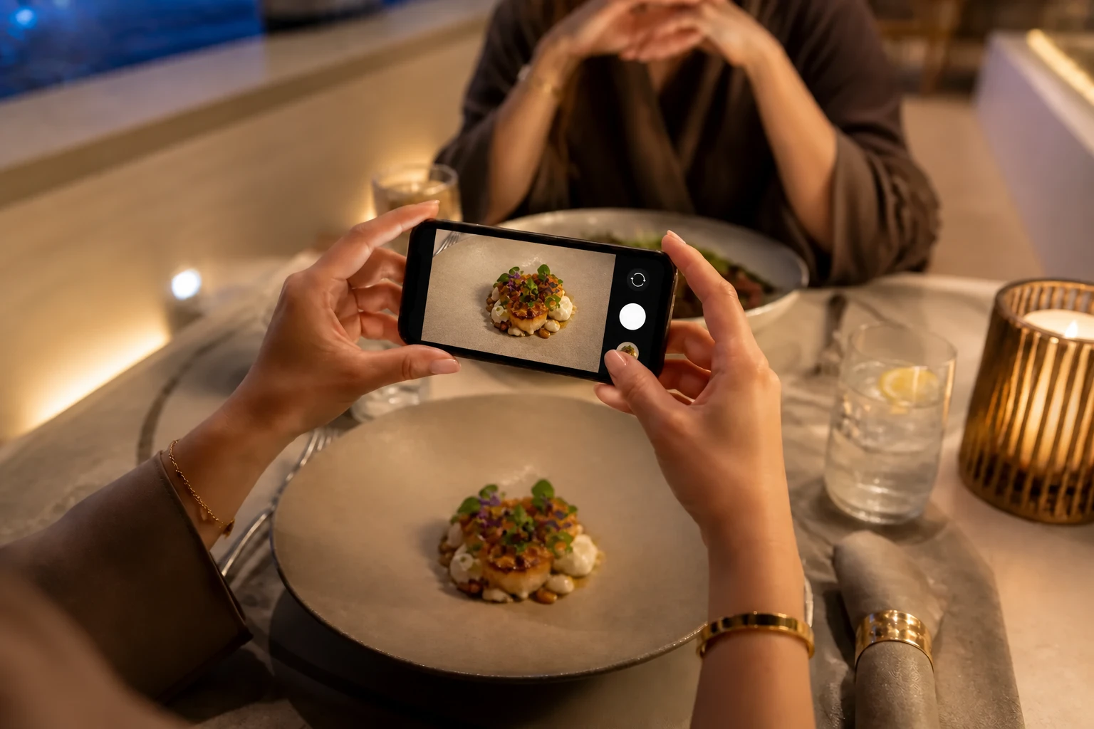 A guest photographing a plated dish with a smartphone at a restaurant table.