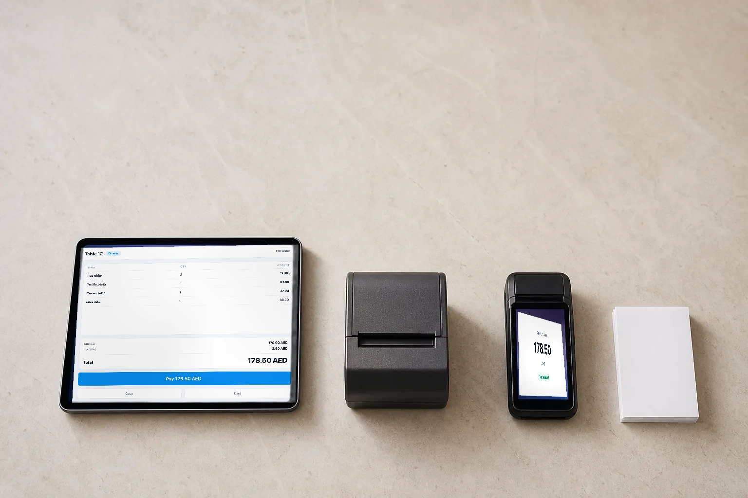 A tablet, receipt printer, and card reader arranged on a pale stone counter in morning light.